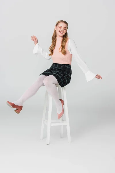 Excited woman in vintage outfit sitting on high stool with closed eyes on grey — Stock Photo