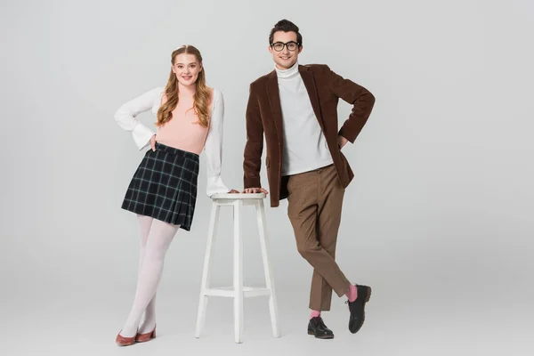 Stylish couple in vintage outfit posing with hands on hips near high stool on grey background — Stock Photo