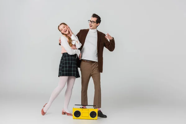Smiling man embracing excited woman near vintage boombox on grey — Stock Photo