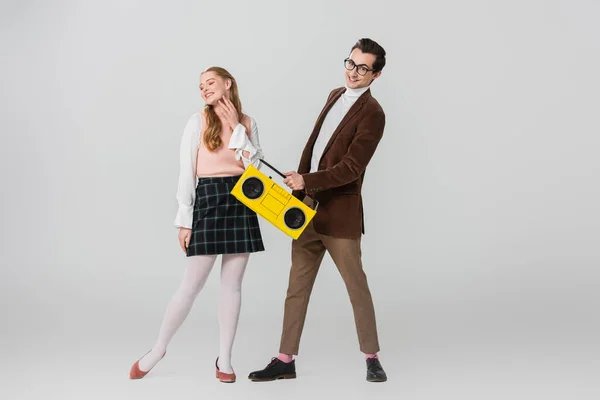 Man holding vintage tape recorder near joyful woman standing with closed eyes on grey — Stock Photo