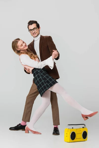 Man looking at camera while dancing with pretty girlfriend near vintage boombox on grey — Stock Photo