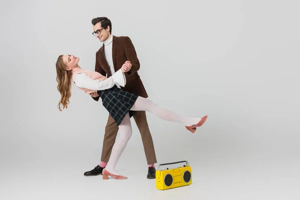 Young couple in retro style clothes dancing near vintage tape recorder on grey — Stock Photo