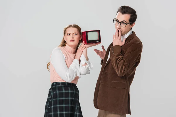 Amazed man covering mouth with hand near discouraged woman with vintage tv isolated on grey — Stock Photo