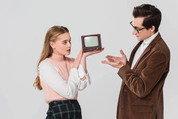 Чоловік вказує на старовинний телевізор в руках здивованої жінки ізольовано на сірому — стокове фото