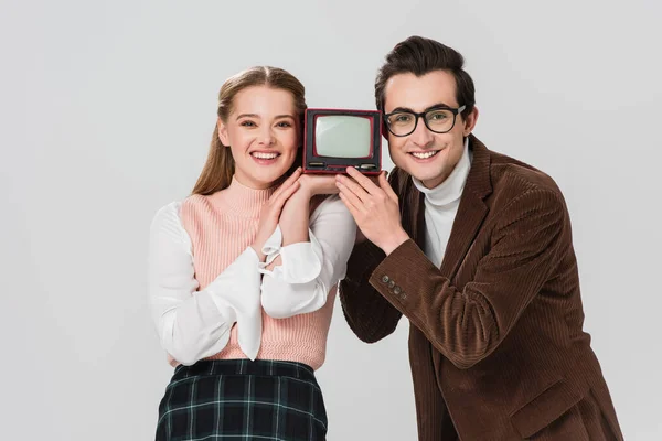 Happy couple looking at camera while holding portable vintage tv isolated on grey — Stock Photo