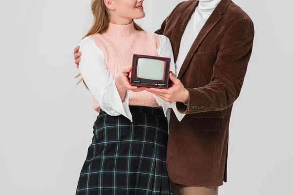 Partial view of stylish couple holding portable vintage tv isolated on grey — Stock Photo