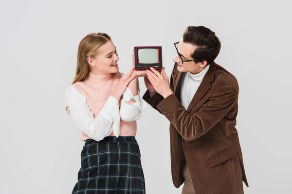 Sonriente pareja en retro traje celebración pequeño vintage tv aislado en gris — Stock Photo