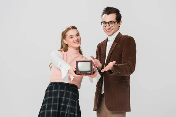 Man in eyeglasses pointing at vintage tv in hands of cheerful woman isolated on grey — Stock Photo