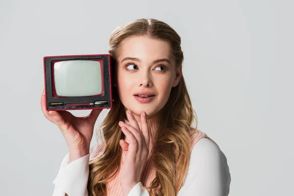 Femme rêveuse toucher le menton et regarder loin tout en tenant petite télévision vintage isolé sur gris — Photo de stock