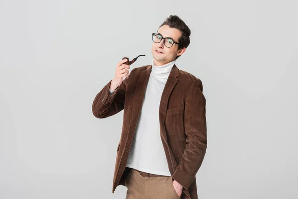 Stylish man in old fashioned blazer smoking pipe while posing with hand in pocket isolated on grey — Stock Photo