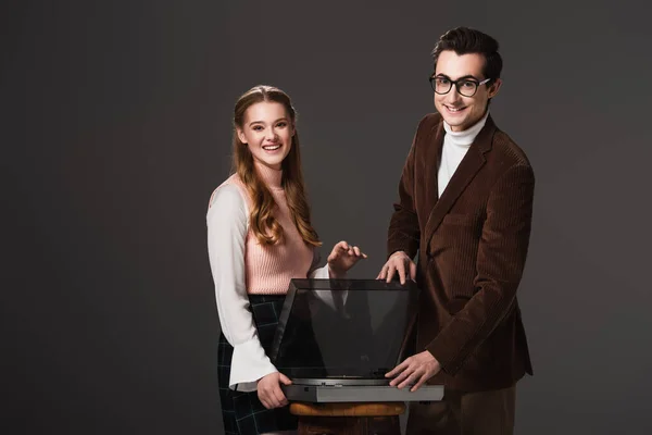 Happy couple in vintage clothes looking at camera near vinyl player isolated on black — Stock Photo