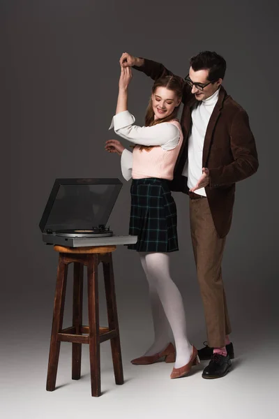 Elegante, pareja de moda bailando cerca de vinilo jugador sobre fondo gris oscuro - foto de stock