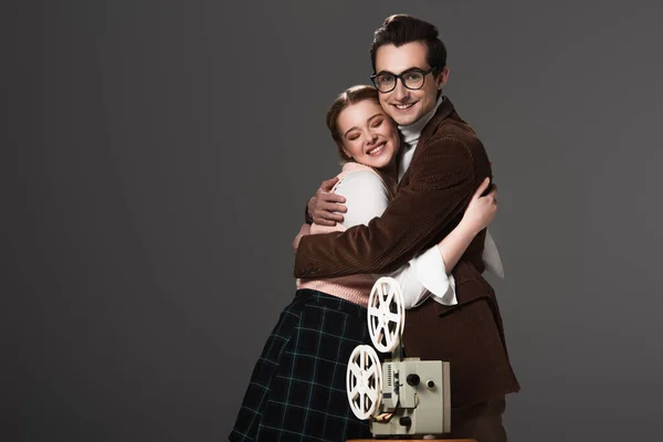 Glückliches altmodisches Paar umarmt nahe Filmprojektor isoliert auf schwarz — Stockfoto