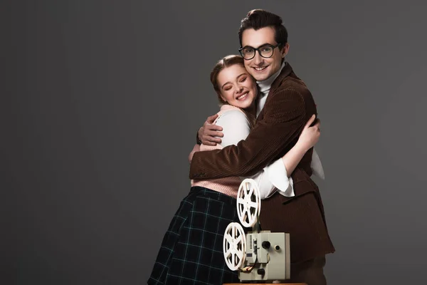 Happy old fashioned couple embracing near movie projector isolated on black — Stock Photo