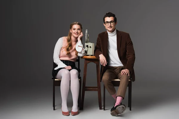 Smiling couple in vintage clothes watching movie on film projector on grey background — Stock Photo