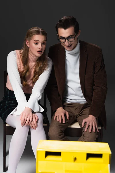 Donna stupita guardando la tv vicino sorridente uomo su sfondo grigio scuro — Foto stock