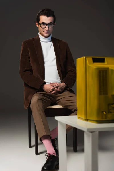 Young man in vintage outfit watching movie while sitting on dark grey background — Stock Photo