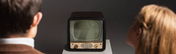 Rückansicht von verschwommenen Mann und Frau, die Vintage-Fernseher isoliert auf grau sehen, Banner — Stockfoto