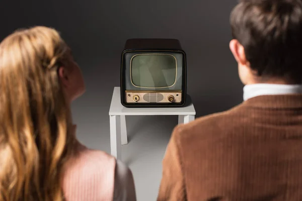 Вид ззаду розмита пара дивиться ретро телевізор на сірому фоні — стокове фото