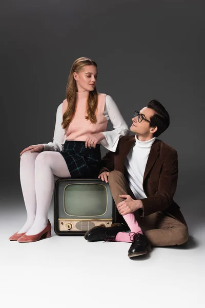 Altmodisches Paar, das sich in der Nähe von Vintage-TV auf grauem Hintergrund anschaut — Stockfoto
