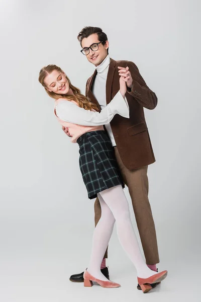 Young man smiling at camera while dancing with happy girlfriend on grey — Stock Photo