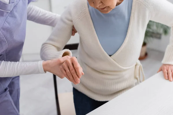 Cropped view of social worker helping senior woman getting up — Stock Photo