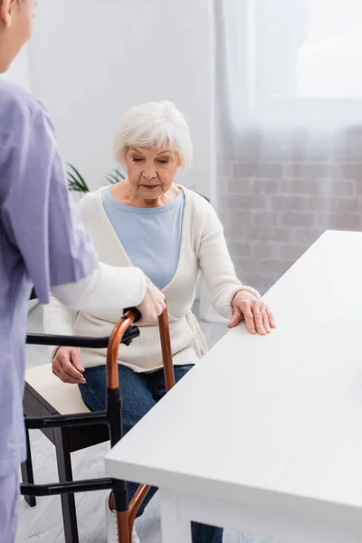 Nurse giving medical walkers to senior woman sitting in kitchen — Stock Photo