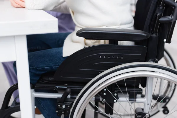 Vue recadrée de la femme handicapée âgée assise en fauteuil roulant près de la table — Photo de stock