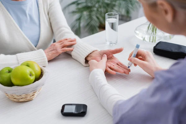 Visión parcial de la enfermera inyectando insulina a una mujer diabética de edad avanzada cerca del glucosímetro, borrosa en primer plano - foto de stock