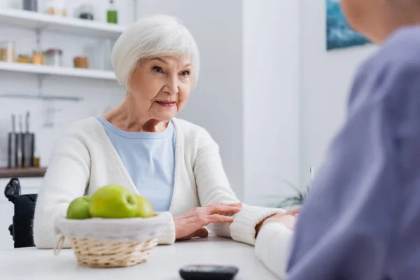 Senior diabetic woman looking at social worker near blurred glucometer — Stock Photo