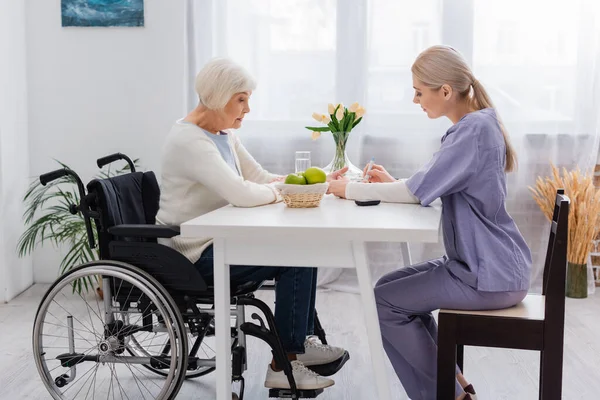 Vue latérale de l'infirmière qui injecte de l'insuline à une aînée handicapée en fauteuil roulant — Photo de stock