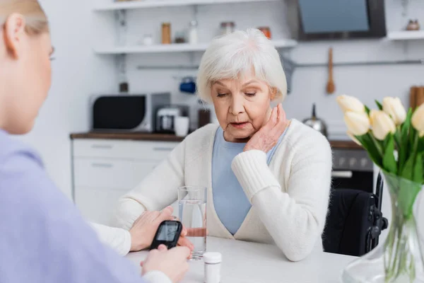Enfermeira com glicosímetro tocando a mão da mulher diabética sênior, foreground borrado — Fotografia de Stock