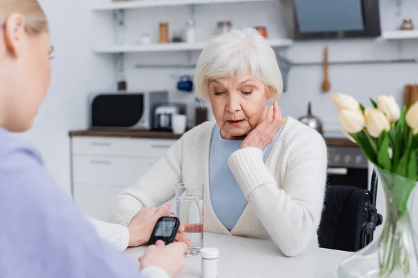 Krankenschwester mit Glukometer, die Hand einer älteren Diabetikerin berührend, verschwommener Vordergrund — Stockfoto