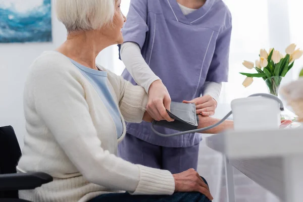 Ausgeschnittene Ansicht einer Krankenschwester, die den Blutdruck einer älteren Frau zu Hause misst — Stockfoto