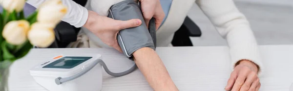 Ausgeschnittene Ansicht eines Sozialarbeiters, der einer Seniorin Manschette mit Tonometer an die Hand legt, Banner — Stockfoto