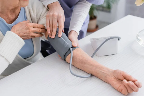 Ausgeschnittene Ansicht einer Sozialarbeiterin, die den Blutdruck einer Seniorin mit einem Tonometer misst — Stockfoto