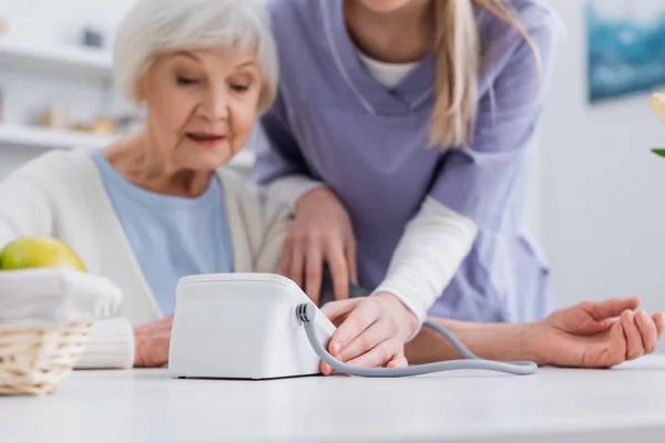 Selective focus of tonometer near elderly woman and nurse on blurred background — Stock Photo