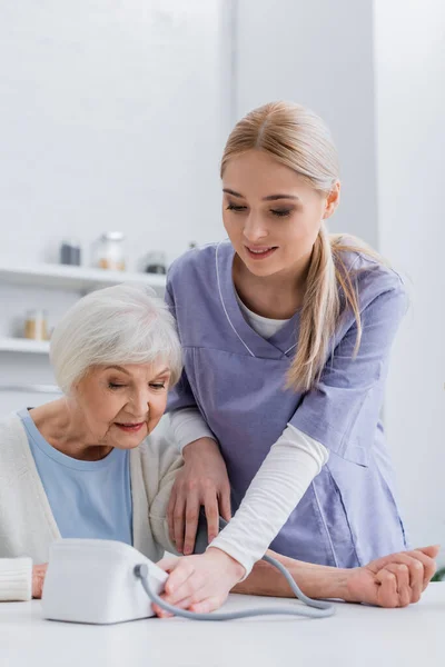 Enfermeira sorrindo medir a pressão arterial de mulher idosa com tonômetro — Fotografia de Stock