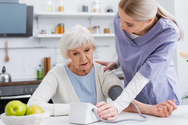 Junge Krankenschwester berührt Schulter einer Seniorin, während sie ihren Blutdruck misst — Stockfoto