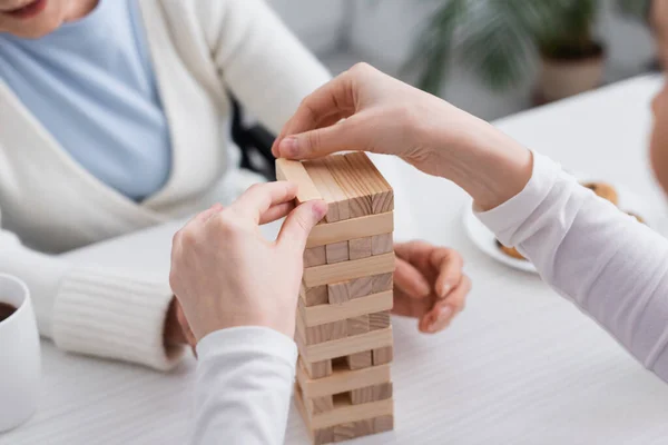 Vista parcial de la enfermera jugando bloques de madera juego con la mujer de edad sobre fondo borroso - foto de stock