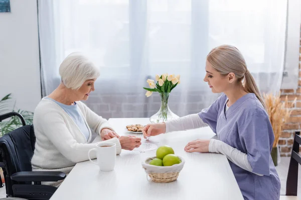 Young social worker playing jigsaw puzzle with handicapper senior woman at home — Stock Photo