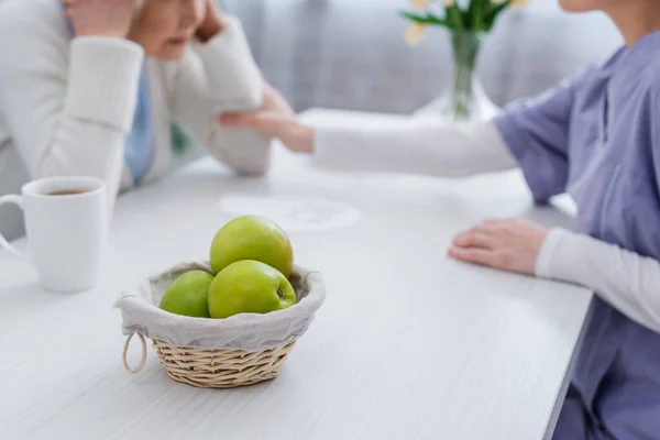 Foyer sélectif de pommes fraîches près de l'infirmière apaisant femme âgée malade sur la démence, vue cultivée — Photo de stock