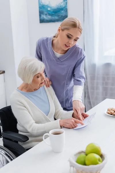 Assistente sociale che indica il calendario vicino alla donna anziana malata di demenza — Foto stock