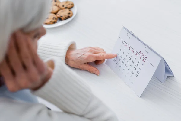 Vue recadrée de la femme âgée, souffrant de perte de mémoire, pointant du doigt le calendrier, premier plan flou — Photo de stock