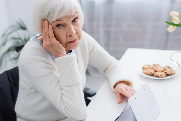 Aged woman, sick on dementia, touching head while looking at camera near calendar — Stock Photo