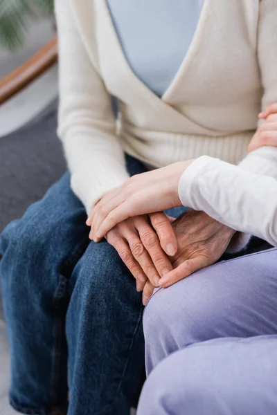 Teilaufnahme einer Krankenschwester, die neben einer Seniorin sitzt und ihre Hand berührt, verschwommener Hintergrund — Stockfoto