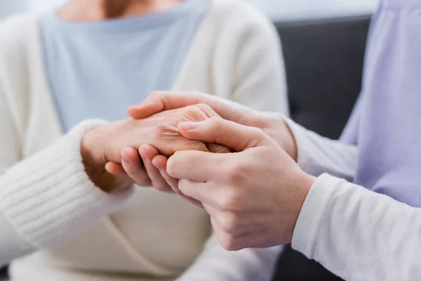 Visión parcial de la enfermera cogida de la mano de una anciana, fondo borroso - foto de stock