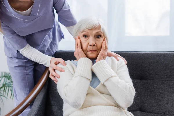 Aged woman, sick on amnesia, holding hands near face while social worker touching her shoulders — Stock Photo