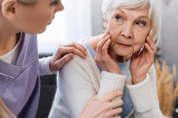 Social worker touching shoulder of senior woman suffering from amnesia, blurred foreground — Stock Photo