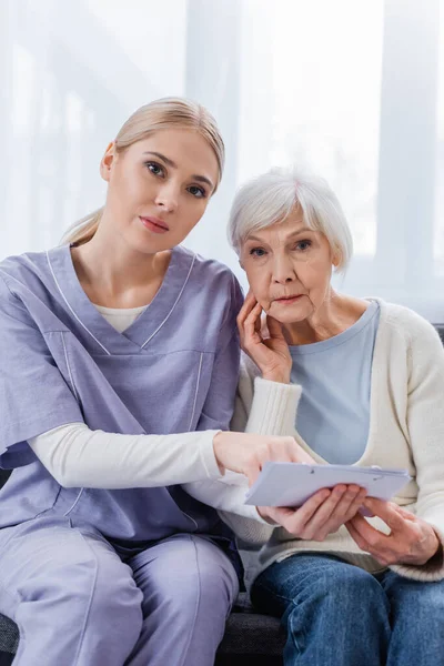 Junge Krankenschwester und Seniorin, an Demenz erkrankt, blickt in die Kamera, während sie den Kalender in der Hand hält — Stockfoto